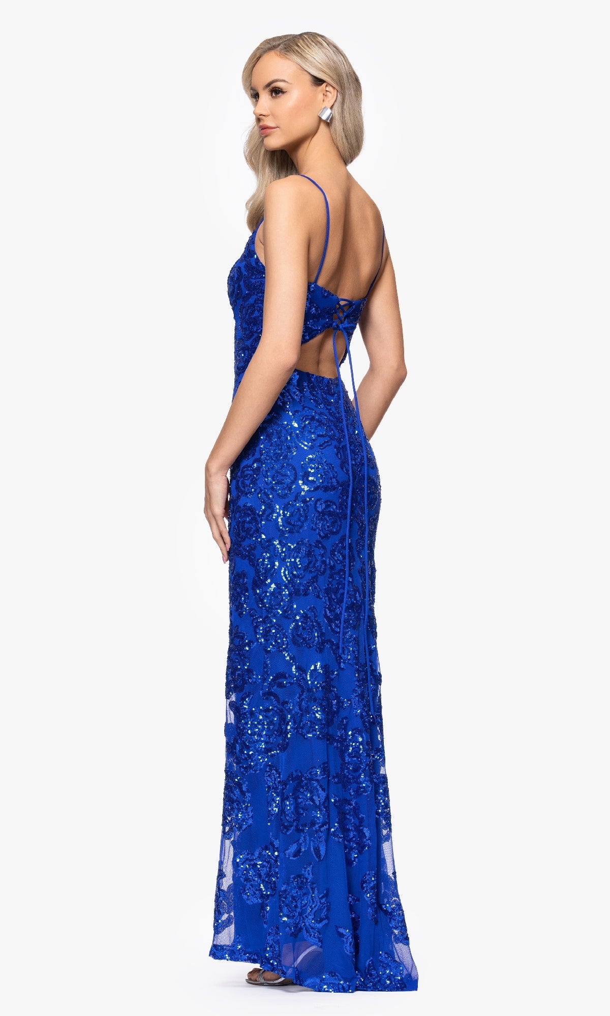 Woman wearing the Long Blue Sequin Prom Dress Blondie Nites 4793BN, featuring spaghetti straps and an open back, standing against a plain white background.